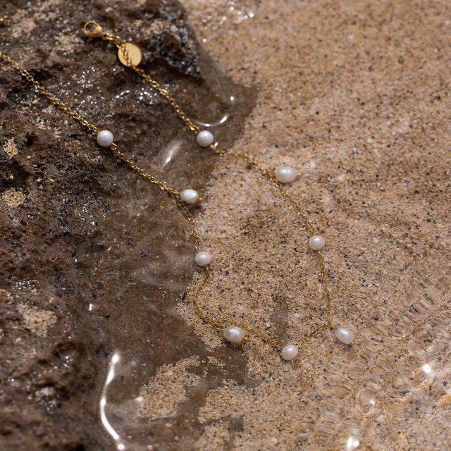 Pearl Drop Fußkettchen von PURELEI mit goldener Kette und zarten Süßwasserperlen, elegant im Sand arrangiert.