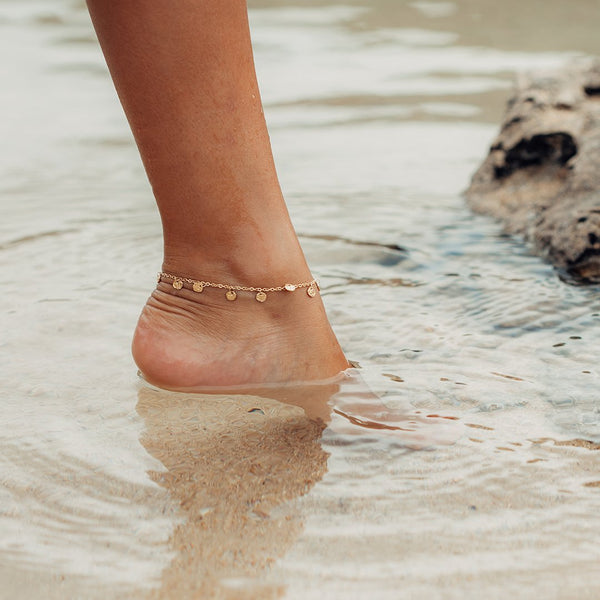 PURELEI Malihini Coin Fusskettchen aus 18K vergoldetem Edelstahl, wasserfest und elegant am Fuß im klaren Wasser.