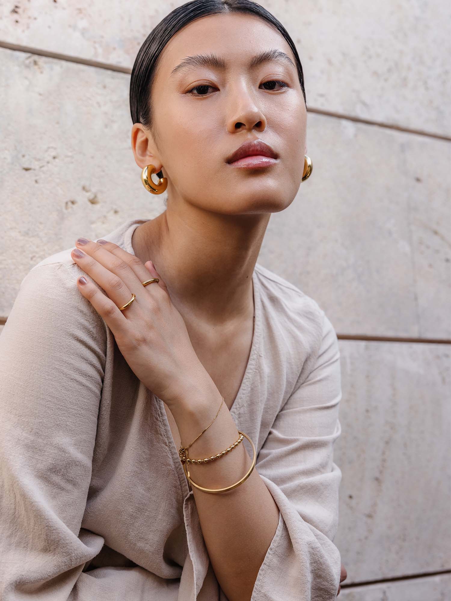 Elegante goldene Creolen und zarte Ringe von PURELEI, getragen in minimalistischer Atmosphäre.