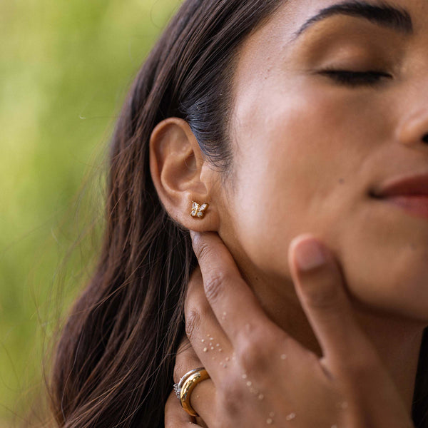 Goldene Schmetterlingsohrstecker von PURELEI, elegant und feminin, umgeben von natürlicher Schönheit.
