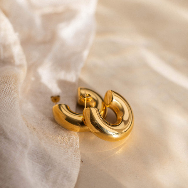 Goldene Creolen von PURELEI auf sanftem Stoff, strahlend und elegant.