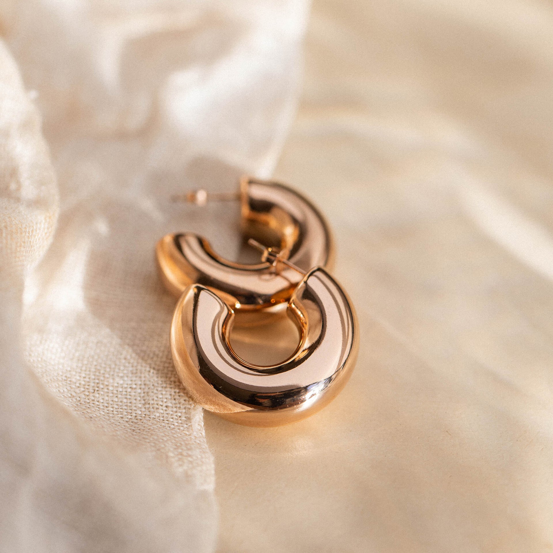 Goldene Creolen von PURELEI auf sanftem Stoff, elegant und modern.