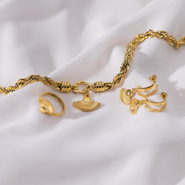 PURELEI Breeze Charm Anhänger in 18K Gold mit Fächerdesign, auf edlem weißen Stoff inszeniert.