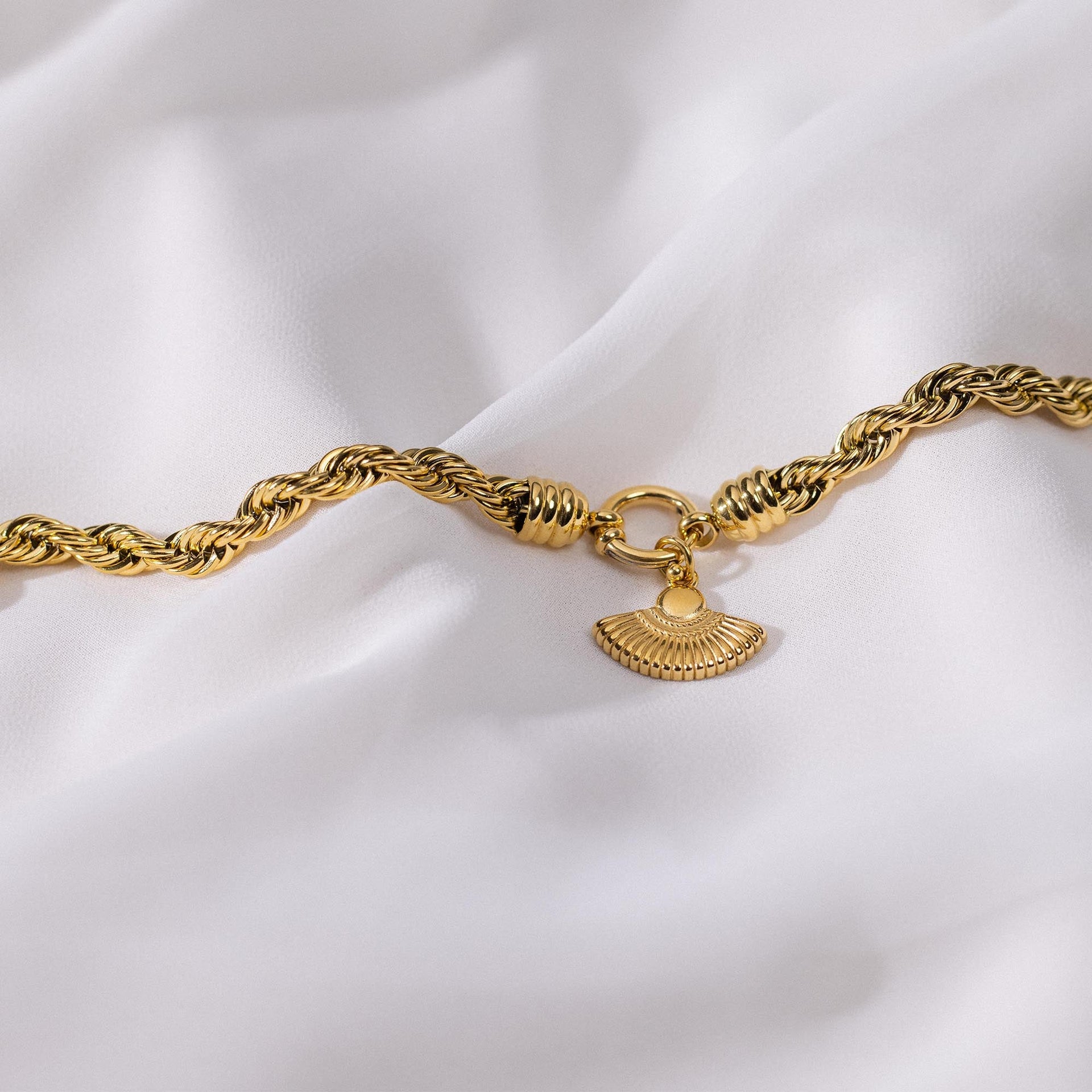 Goldene Kette mit geflochtenem Design und Muschel-Anhänger, PURELEI auf sanftem Stoff.